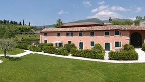 A pink villa with a tiled roof, surrounded by well-maintained lawns and hedges, set against a backdrop of hills and trees. - I Cortivi 2   Montebaldo (Costermano)