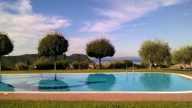 A rectangular swimming pool with a clear blue water surface, surrounded by a brick pathway and lush green grass. - I Cortivi 2   Montebaldo (Costermano)