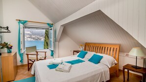 A bedroom with a sloped ceiling, a bed with blue bedding, a wooden headboard, a nightstand, a lamp, a chair, a desk, and a window with a view of a snowy landscape. - Beautiful shoreline holiday home with private mooring, Njivice, Montenegro (Njivice)