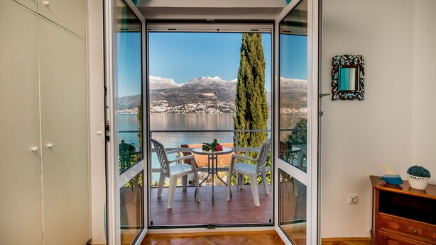 A balcony with a table and chairs, a potted plant, and a view of a lake and mountains. - Beautiful shoreline holiday home with private mooring, Njivice, Montenegro (Njivice)