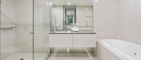 A modern bathroom with a glass shower enclosure, a white sink with a mirror above, and a standalone bathtub.