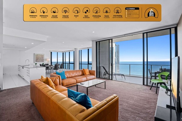 A modern hotel room with a large balcony, a sofa, a dining area, and a kitchen.