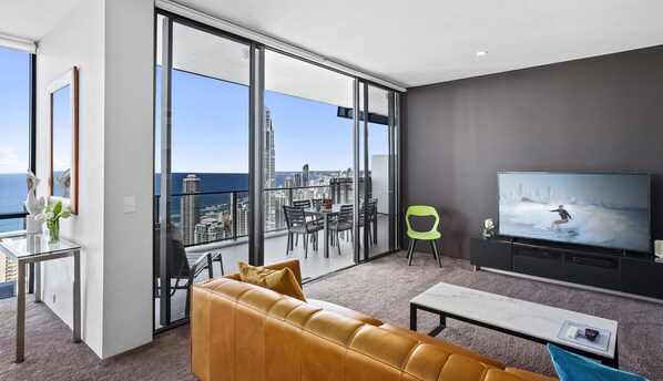 A modern living room with a large TV, a sofa, and a balcony with a city view.