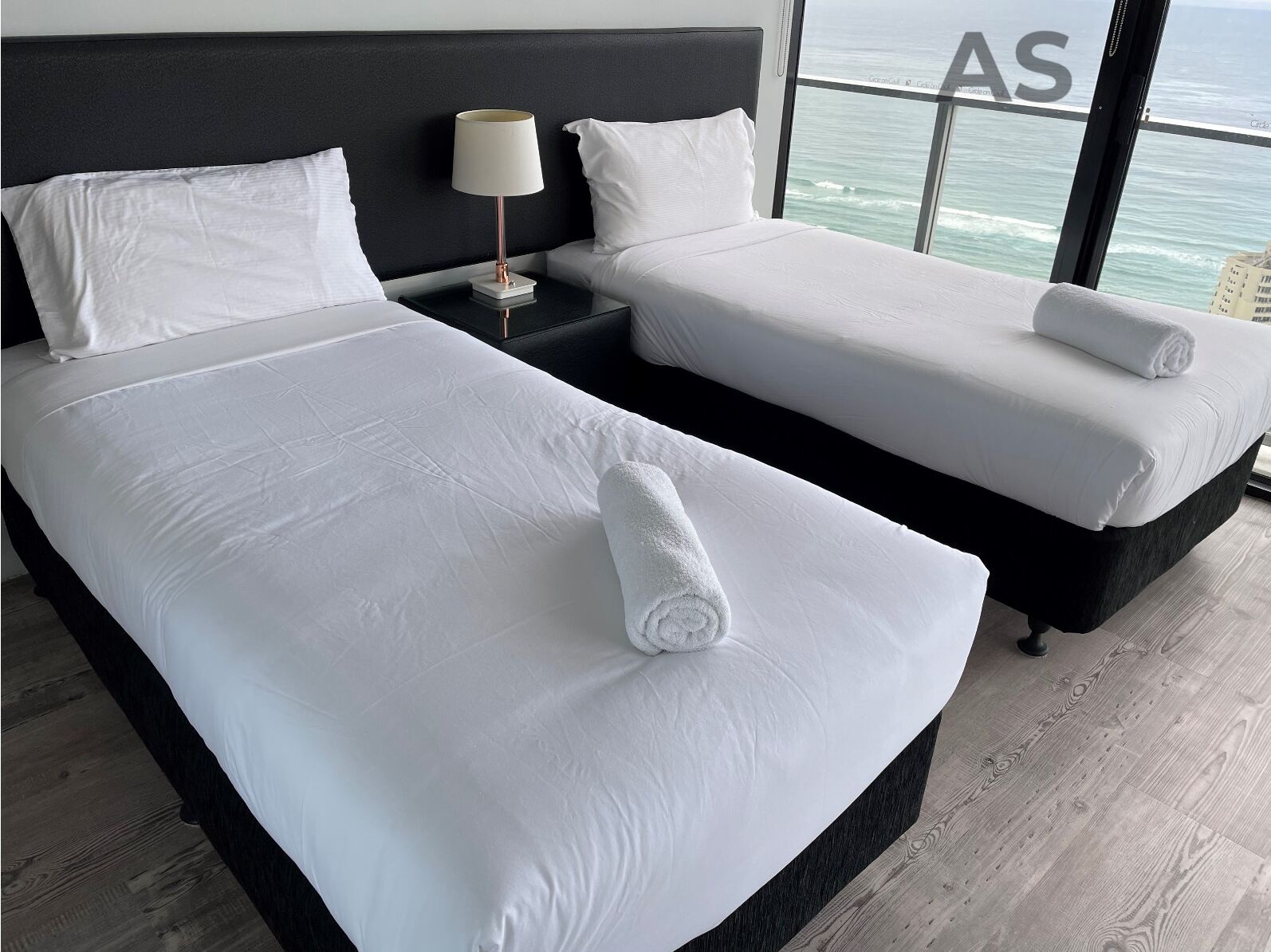 A hotel room with two beds, a nightstand with a lamp, and a view of the ocean.