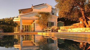 Une maison à deux étages dotée d’un balcon, d’une piscine et d’un mur en pierre agrémenté d’une rampe décorative.
