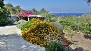Un jardin avec un sentier en pierre, des plantes en fleurs et une vue sur la mer.