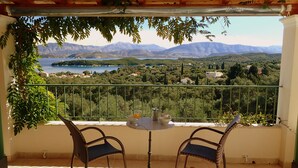Un balcon avec des fauteuils en osier, une petite table ronde et une vue sur un lac et des montagnes.