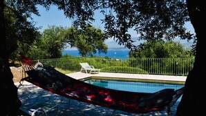 Un hamac suspendu au-dessus d’une piscine, avec vue sur la mer et une clôture verte.