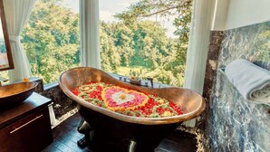A bathroom with a freestanding bathtub filled with flower petals, a wooden basin, and a view of lush greenery through large windows. - Villa Kalisha - Romantic Honeymoon or Family Getaway in Ubud (Tegallalang)