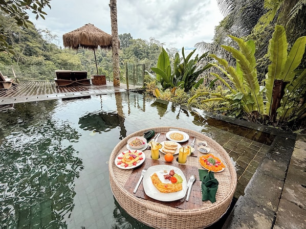 A dining setup by a pool with a wicker table, plates of food, and drinks.