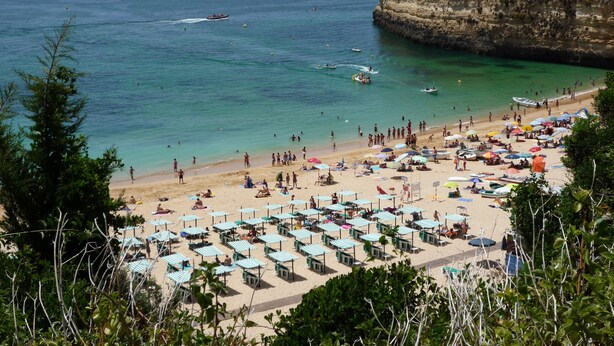 A beach with numerous umbrellas and sun loungers, a rocky cliff with a small building, and boats in the water. - Apartment in resort 3* at 1mn to the beach - Algarve (Porches)