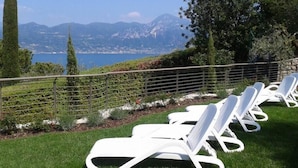 A row of white lounge chairs on a grassy lawn with a view of mountains and a lake.