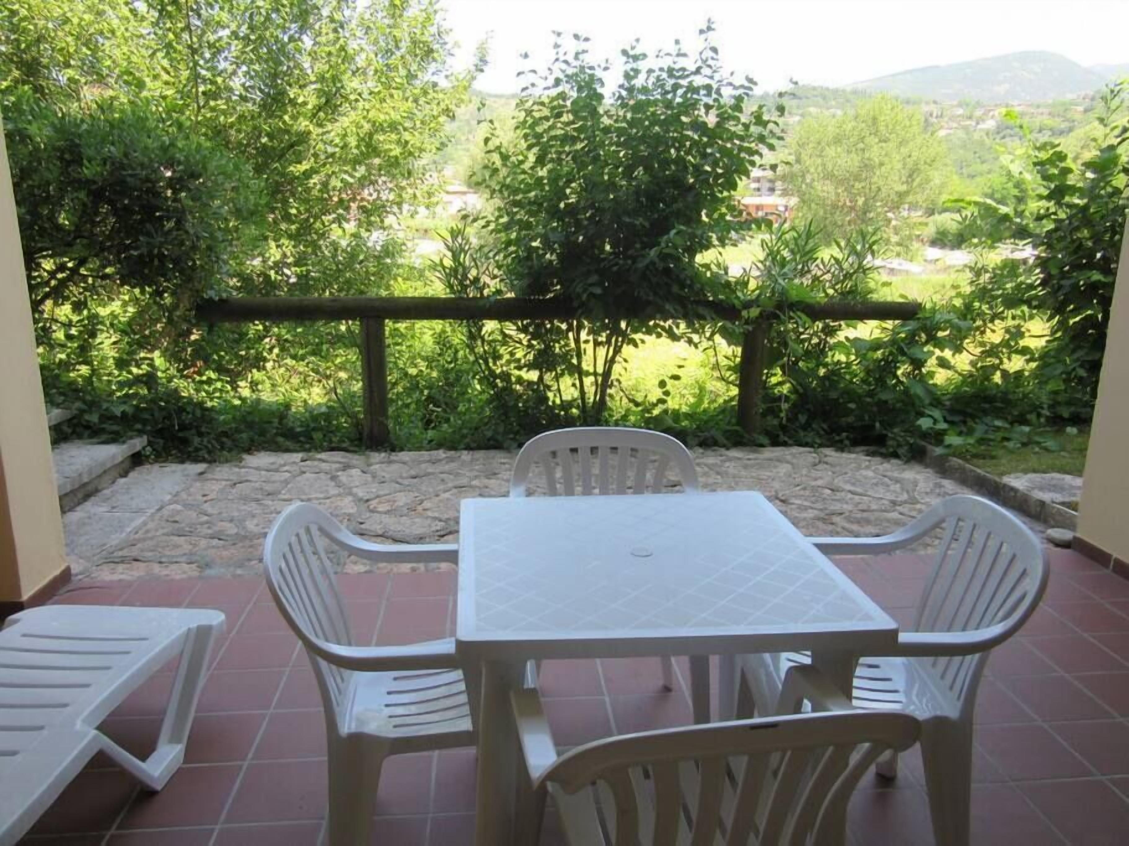 Um pátio com uma mesa e quatro cadeiras, cercado por muros de pedra e vegetação.