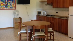 A compact kitchen with wooden cabinets, a microwave, a stove, and a dining table with chairs. - Garda Residences   Le Rasole Economy (Garda)