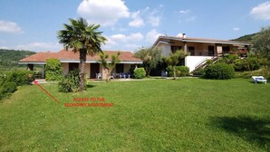A two-story building with a red-tiled roof, a covered patio area, and a well-maintained lawn. - Garda Residences   Le Rasole Economy (Garda)