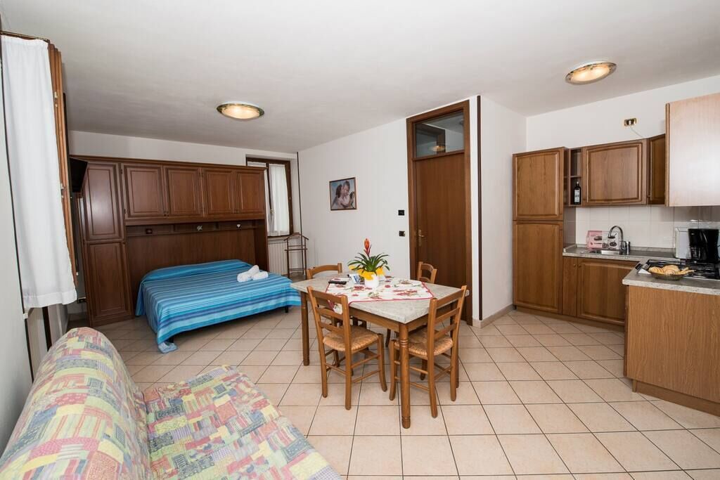 A compact room with a bed, a dining table with chairs, a kitchenette, and wooden cabinets.