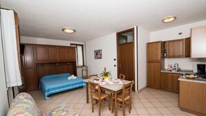 A compact room with a bed, a dining table with chairs, a kitchenette, and wooden cabinets.