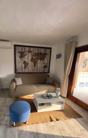 A living room with a sofa, a coffee table, a blue ottoman, a world map artwork, and a window with curtains.