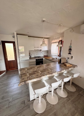 Une cuisine moderne avec des meubles blancs, un pare-feu en marbre, une cuisinière à gaz et un coin bar avec des tabourets.