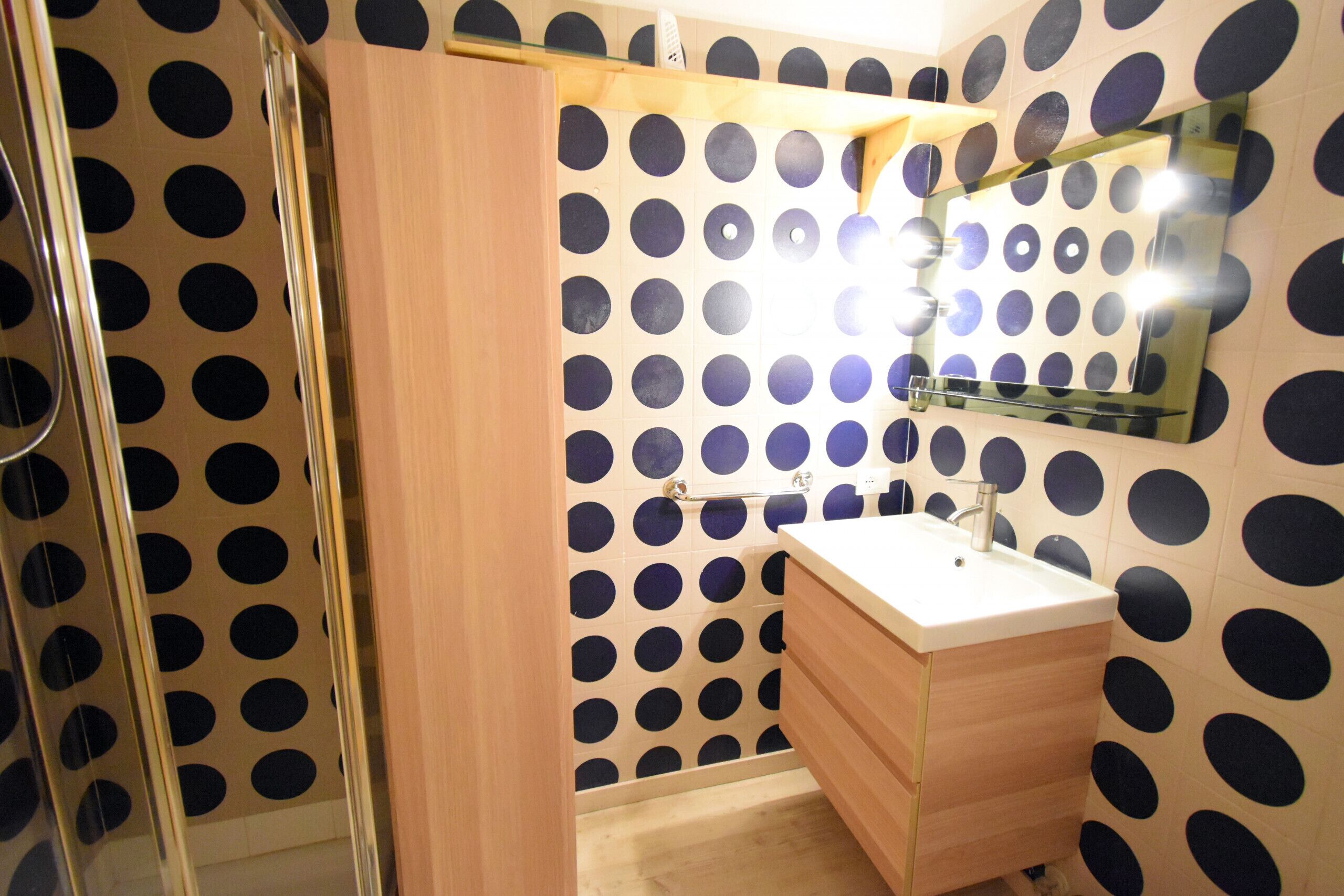 A bathroom with a polka dot wall design, a wooden vanity, and a glass shower enclosure.