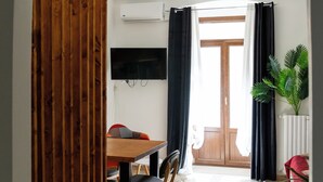 Ein Essbereich mit Holztisch und Stühlen, einem an der Wand montierten Fernseher und einem Blumentopf.
