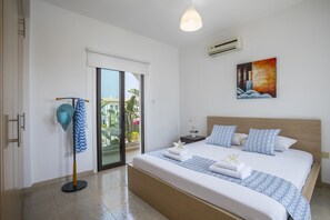 Une chambre d’hôtel avec un grand lit, une vue par une porte coulissante, un ventilateur de plafond et un tableau au mur.