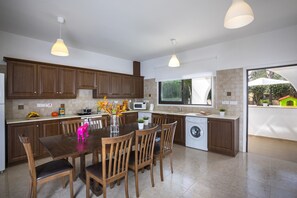 Une cuisine moderne avec des meubles en bois, une table à manger avec des chaises, un lave-linge et une fenêtre donnant sur un paysage verdoyant.