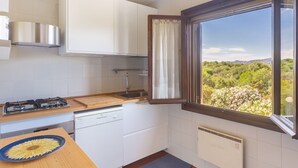 A kitchen with white cabinets, a gas stove, a sink, and a window with a view of greenery.