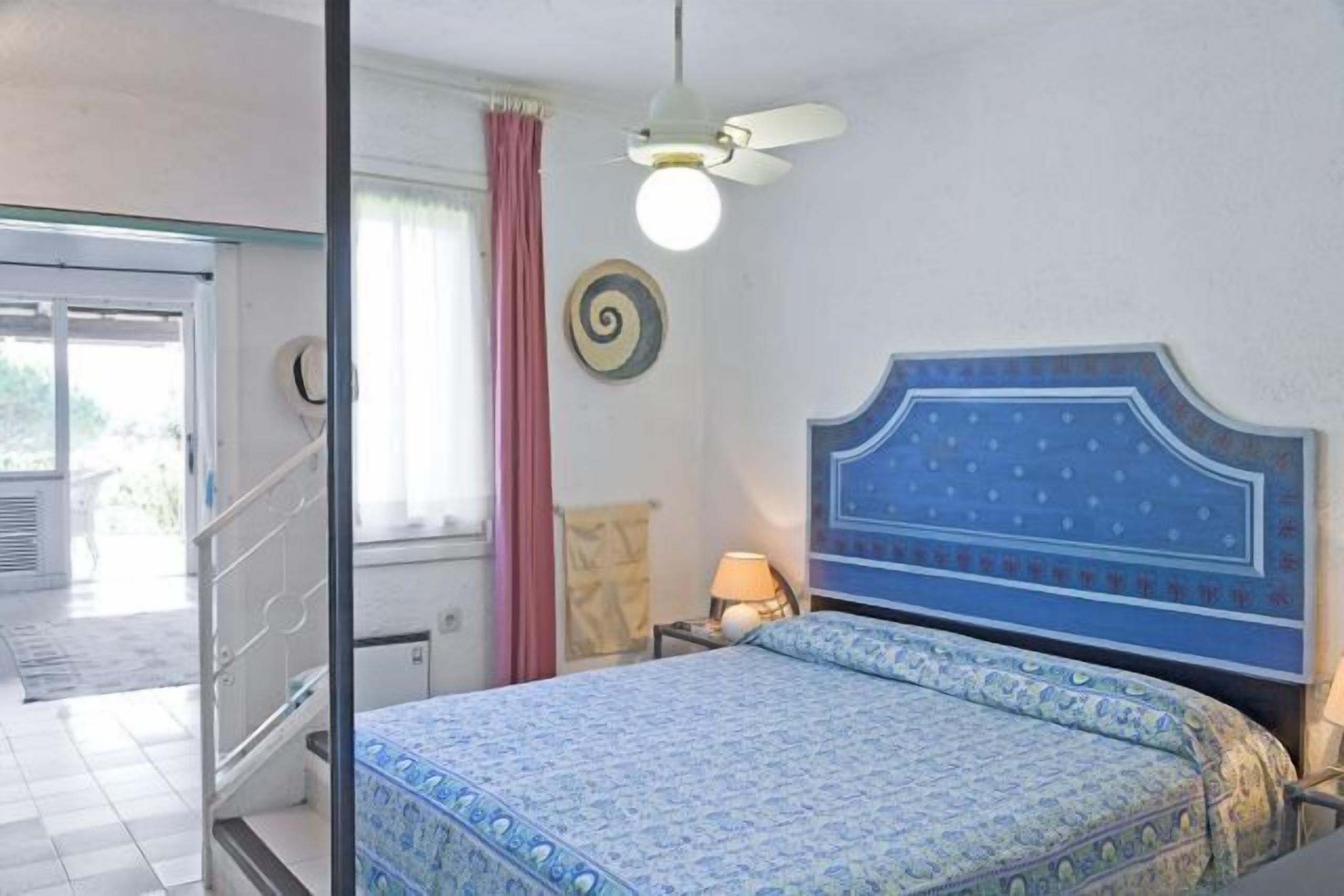 Un dormitorio con cama, ventilador de techo, ventana con cortinas y un reloj de pared.