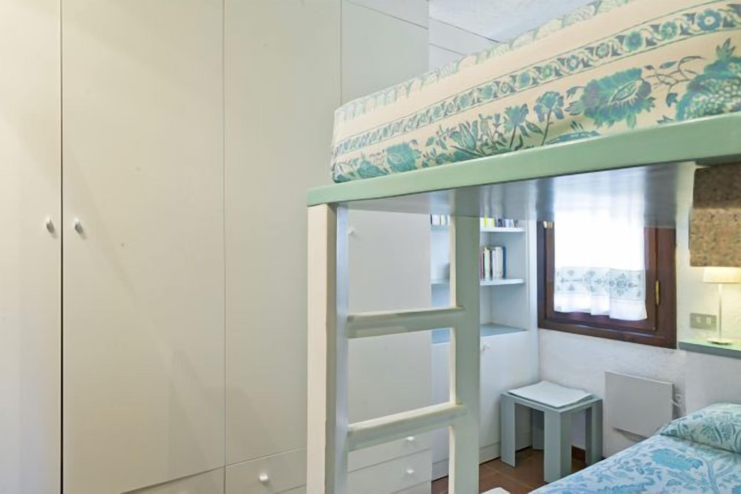 A bedroom with a bunk bed, a small desk, and a window with curtains.