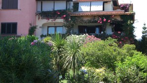 A two-story building with a pink facade, multiple chimneys, and balconies adorned with flowering plants.