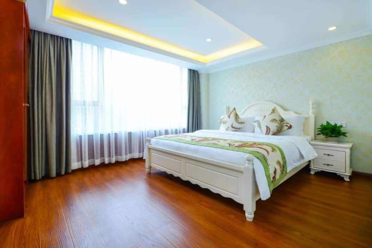 Quarto com uma cama grande, uma mesinha de cabeceira, um criado-mudo e uma janela com cortinas.