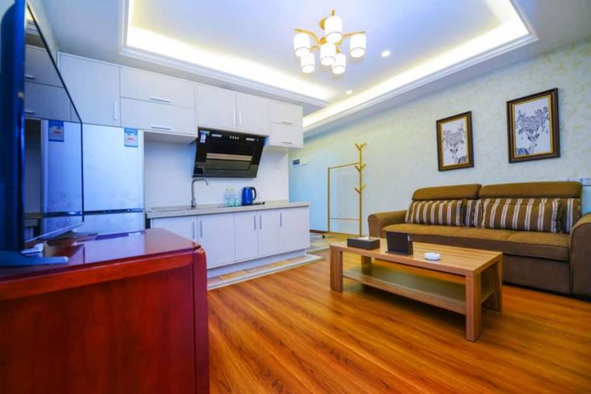 Uma sala de estar moderna com piso de madeira, um sofá, uma mesa de centro e uma área de cozinha com armários brancos e um fogão.
