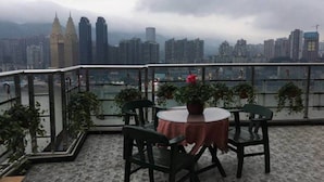 Eine Dachterrasse mit rundem Tisch und Stühlen, Blumentöpfen und Blick auf einen Stadt-Horizont mit hohen Gebäuden.