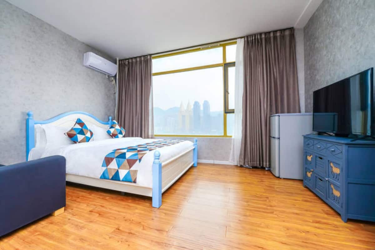 Quarto de hotel moderno com uma cama grande, televisão, cômoda e vista para a cidade.