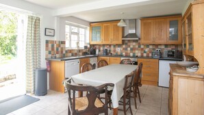 A kitchen with wooden cabinets, a dining table, and various appliances. - Gorgeous thatched cottage in Purbeck - ideal for family holidays (Bere Regis)