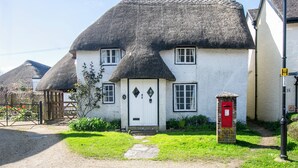 A traditional thatched-roof house with a white exterior, a red mailbox, and a gravel driveway. - Gorgeous thatched cottage in Purbeck - ideal for family holidays (Bere Regis)