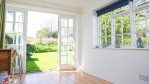 A room with a wooden floor, a desk with drawers, a chair, and a window with a view of a green garden. - Gorgeous thatched cottage in Purbeck - ideal for family holidays (Bere Regis)