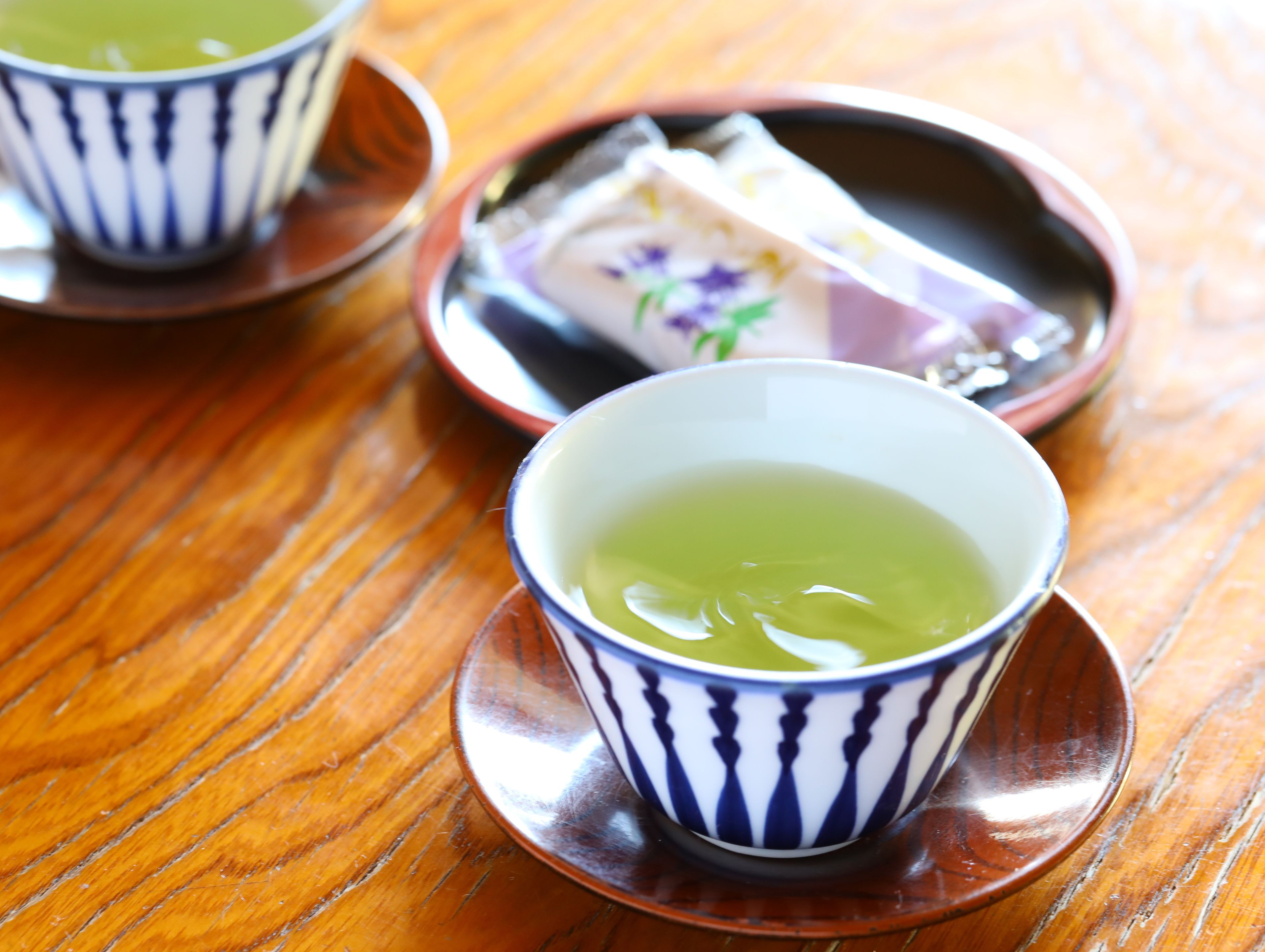 A wooden table with two cups of green tea and a plate with a wrapped item.