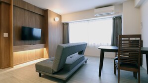 A modern hotel room with a sofa, a dining table, a wooden chair, a flat-screen TV mounted on the wall, and an air conditioning unit. - Shigakogen Hotel Ichibokaku (Yamanouchi)