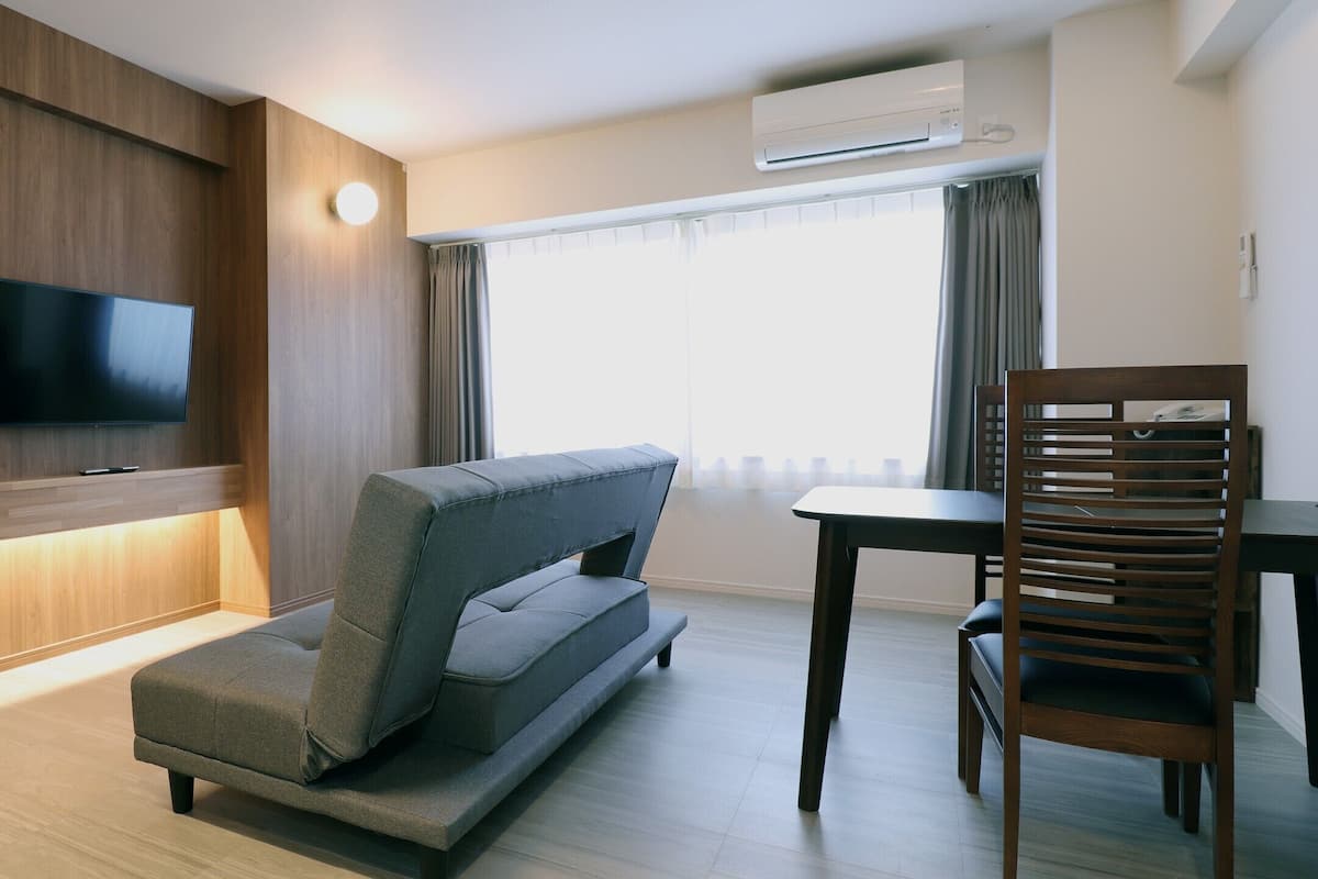 Habitació d'hotel moderna amb un sofà, una taula de menjador, una cadira de fusta, un televisor de pantalla plana fixat a la paret i un aparell d'aire condicionat.