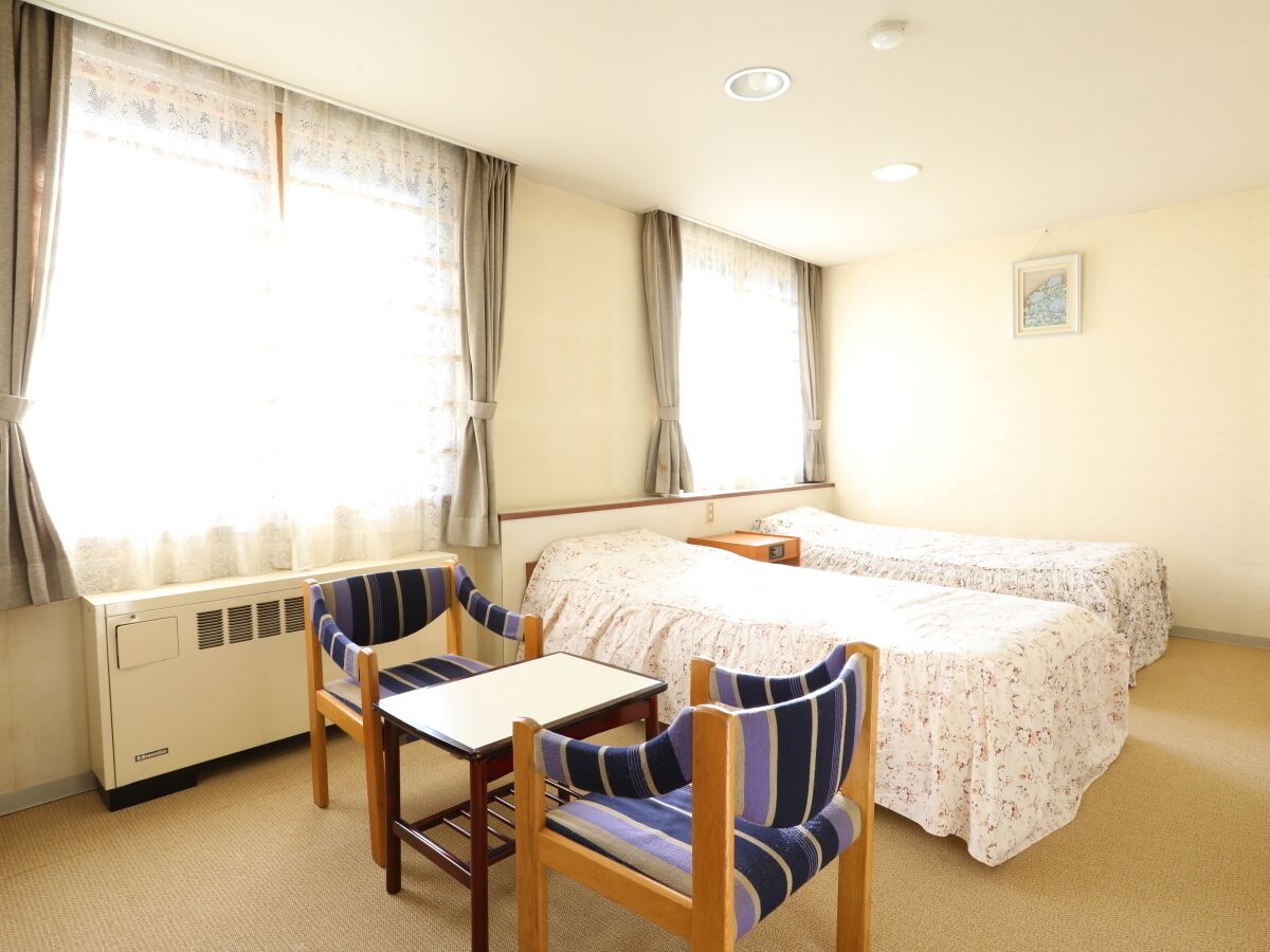 Une petite chambre d’hôtel avec deux lits, une table et deux chaises à rayures.