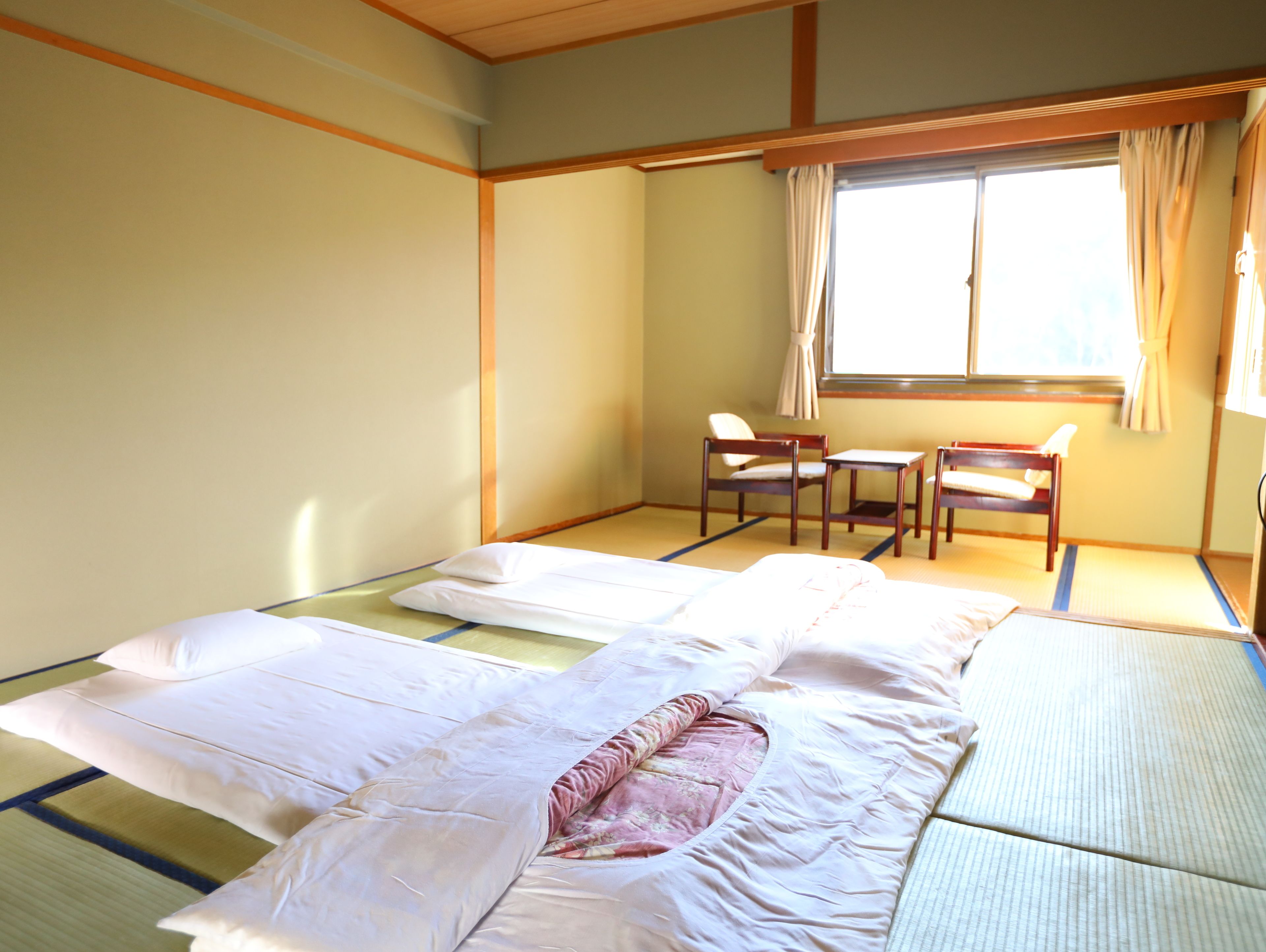 Una tradizionale stanza giapponese con pavimento in tatami, un letto basso in legno, un tavolino e una sedia.