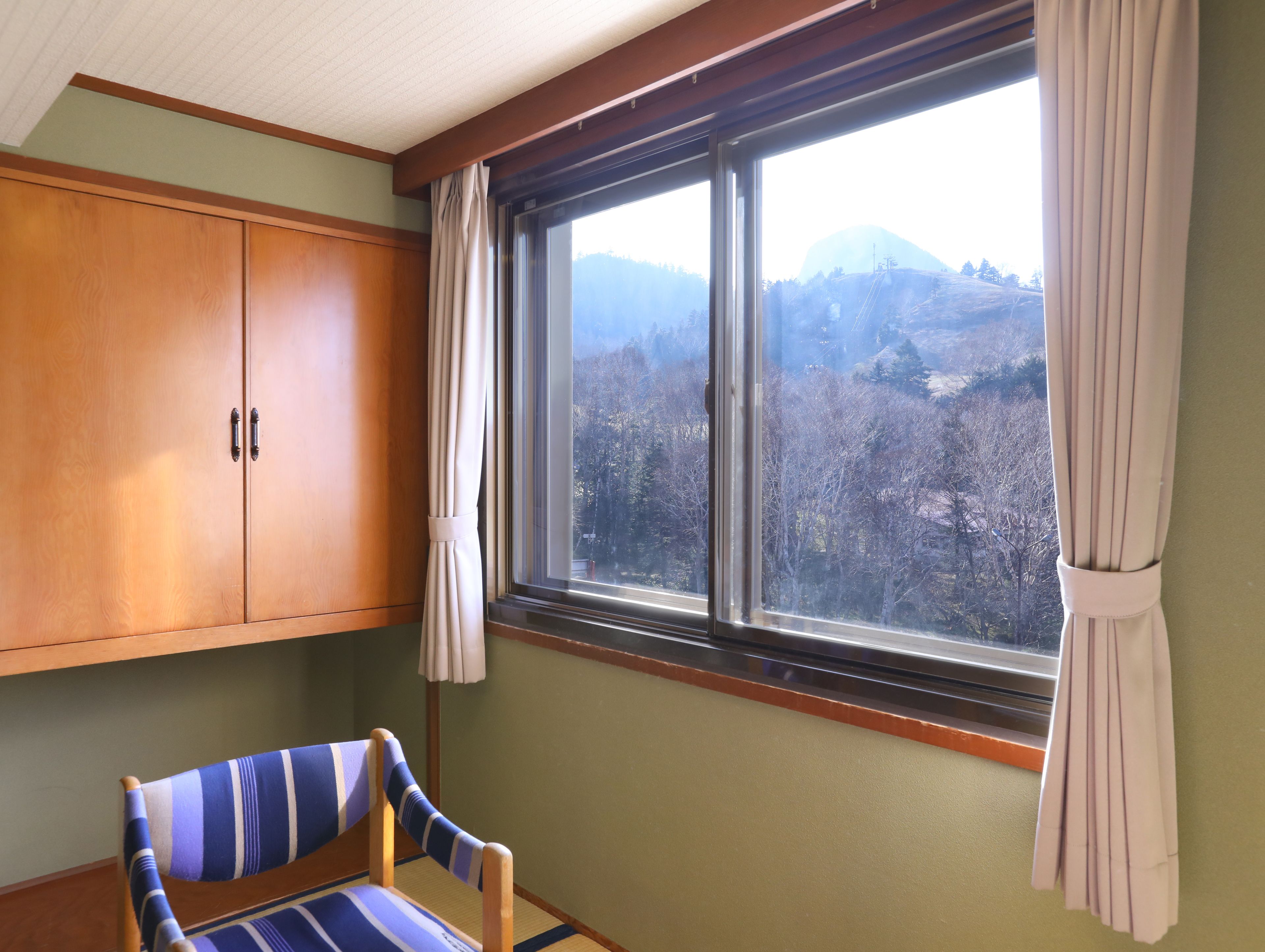 Una habitación con un ventanal grande, un armario de madera y una silla a rayas.