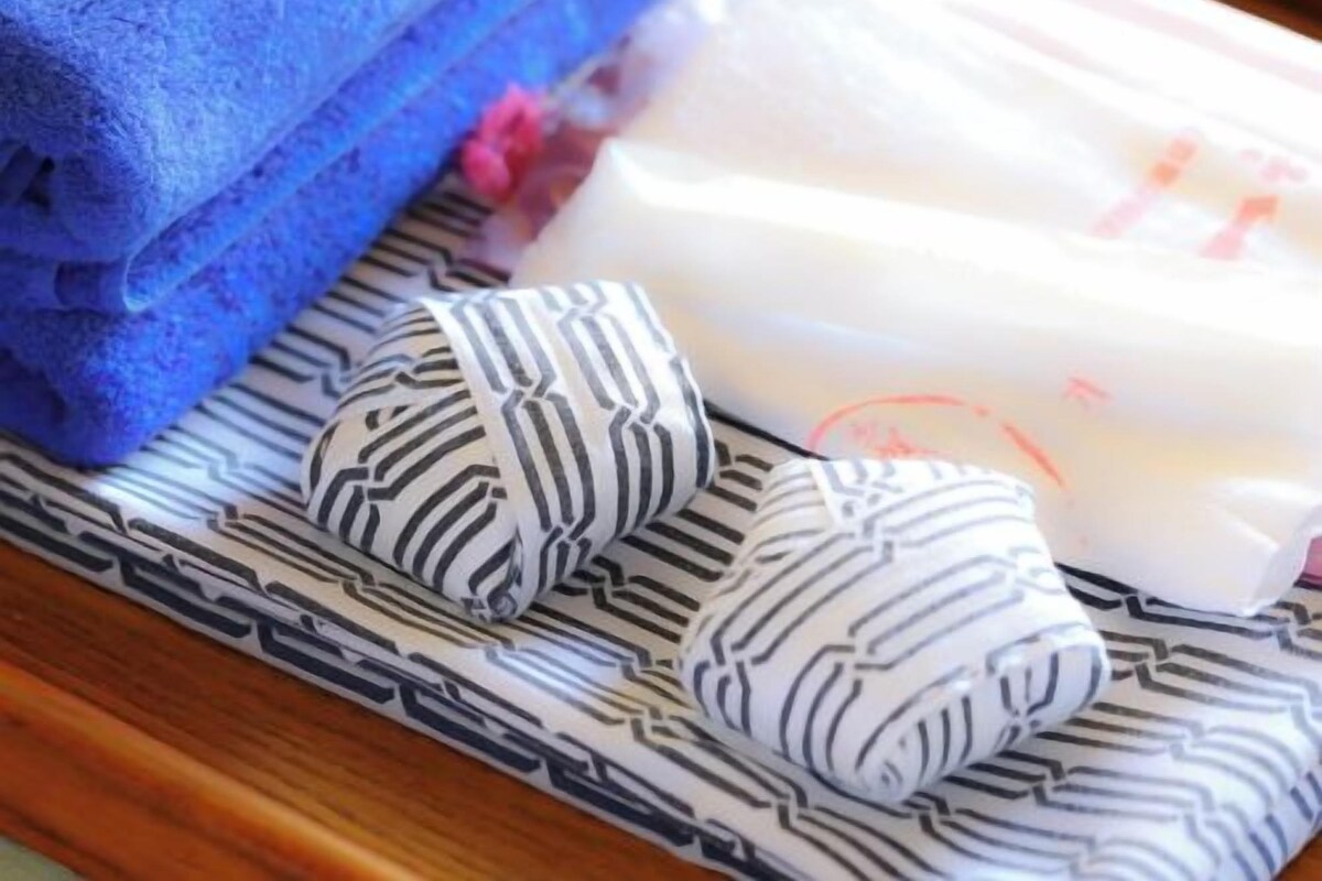 Una toalla azul doblada con cuidado, un cojín a rayas blanco y negro, y un cojín blanco con un diseño rojo sobre una superficie de madera.