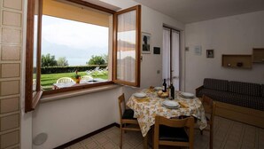 Ein Essbereich mit Tisch für vier Personen, einer Couch und einem Fenster mit Blick auf einen Garten und Berge.