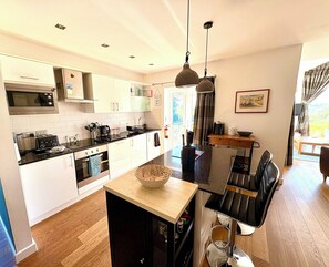 A modern kitchen with a central island, a dining area with a black chair, and a view of the outdoors.