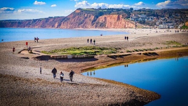 A beach with people walking, a calm sea, and cliffs in the background. - Kokopelli cottage near the Donkey sanctuary Sidmouth , modern and pet friendly. (Sidmouth)