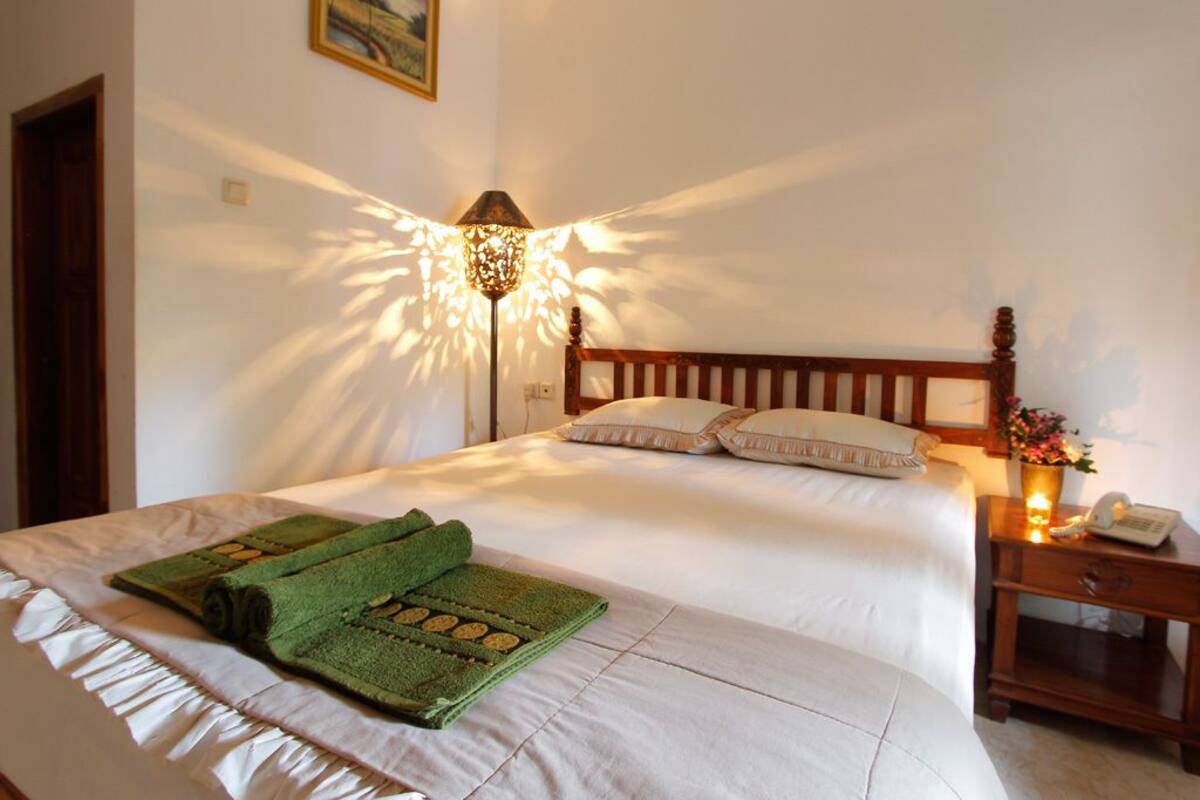 Cama bem arrumada com uma toalha verde e um abajur iluminando a parede.