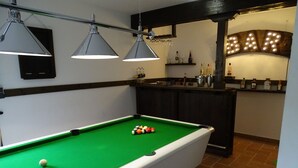 Una mesa de billar con bolas, lámparas colgantes, una zona de bar con botellas y un letrero de bar.
